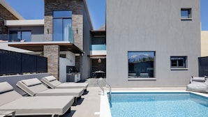 A modern poolside area with lounge chairs, a pool, and a contemporary building with stone and concrete elements. - VillAgioi IIΙ - Stylish Pool Villa, 450m to Sandy Beach (Chania)