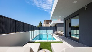 A rooftop pool with clear blue water, surrounded by a modern building with large windows and a view of the sky.