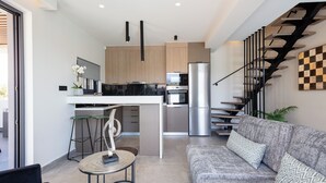 A modern kitchen with a central island, a dining area with a round table, and a grey sofa with patterned cushions.