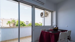 Un balcón con una mesa lista para comer, una ventana con aire acondicionado y vistas a edificios y zonas verdes.
