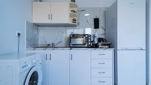 Una cocina moderna con armarios blancos, horno integrado, lavadora y refrigerador.