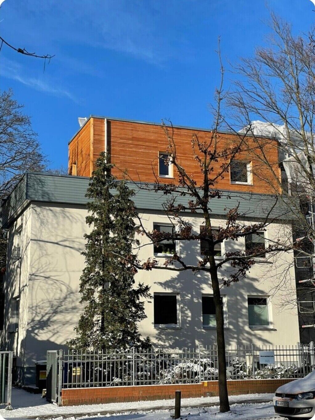 Ein Gebäude mit einem hölzernen Oberteil und einem weißen Unterteil, umgeben von Bäumen und schneebedecktem Boden.