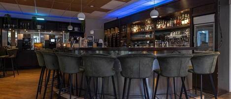 A bar area with a round bar and six stools, a counter with a cash register, and shelves with bottles and glasses.