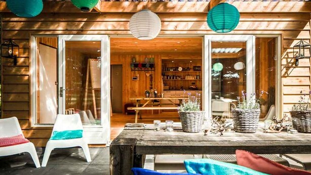 Een terras van hout buiten, met een tafel, stoelen en potplanten.