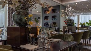 Een restaurant met een donker houten eettafel, omringd door groene bekleden stoelen.