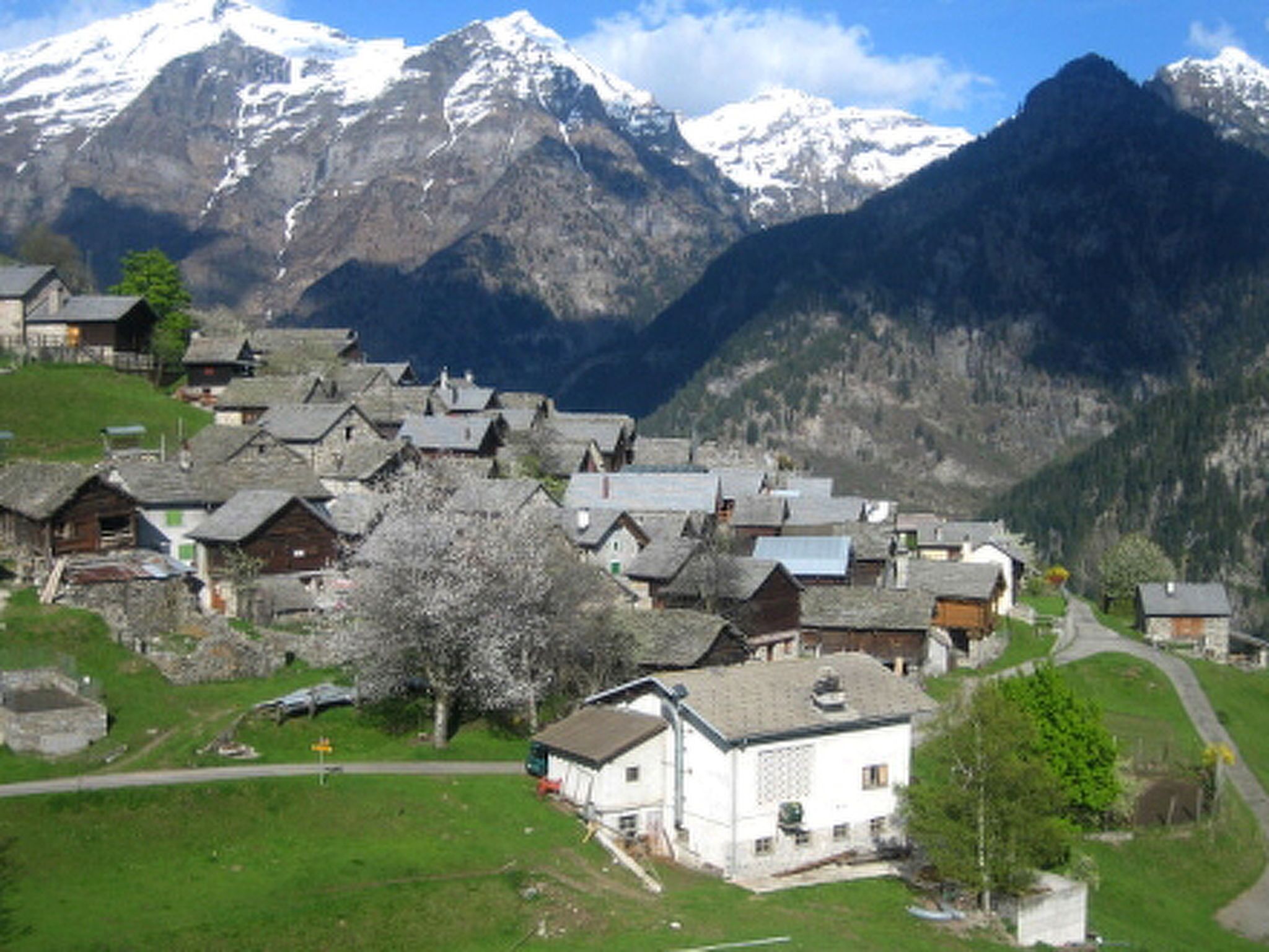 Ein Dorf mit traditionellen Häusern, einer klaren Straße und schneebedeckten Bergen im Hintergrund.