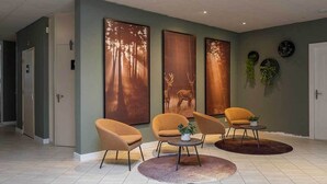 A modern lobby with three large wall-mounted deer paintings, a seating area with three chairs and a round table, and a tiled floor.