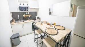 A compact kitchen with a microwave, sink, and a small dining area with a table and stools. - Le Cosy Clim Jardin Parking Privé Tram 20min Plage (Montpellier)