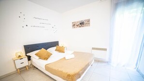 A bedroom with a bed, nightstand, and wall decor. - Le Cosy Clim Jardin Parking Privé Tram 20min Plage (Montpellier)