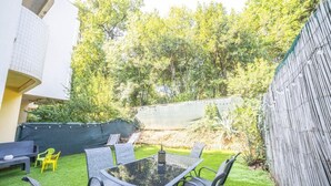 A patio with a glass table and chairs, surrounded by a green lawn and a wooden fence. - Le Cosy Clim Jardin Parking Privé Tram 20min Plage (Montpellier)