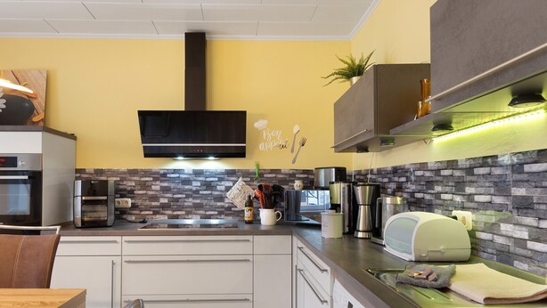 Una cocina moderna con salpicadero de piedra, horno empotrado, cafetera y tostadora.