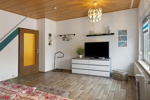Una camera moderna con soffitto in legno, TV a schermo piatto, una pianta in vaso e una mensola a parete.