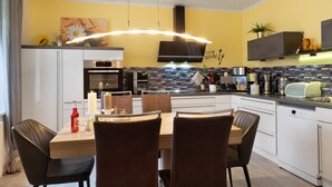 Una cocina moderna con armarios blancos, una mesa de comedor con sillas, horno empotrado y microondas.
