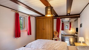 Ein Schlafzimmer mit zwei Betten, einem Holzschrank, einer Hängeleuchte und Blick zur Küche.