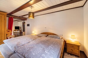 Una camera da letto con soffitto in legno, due letti con lenzuola a motivi, un comodino con una lampada e una tenda rossa.
