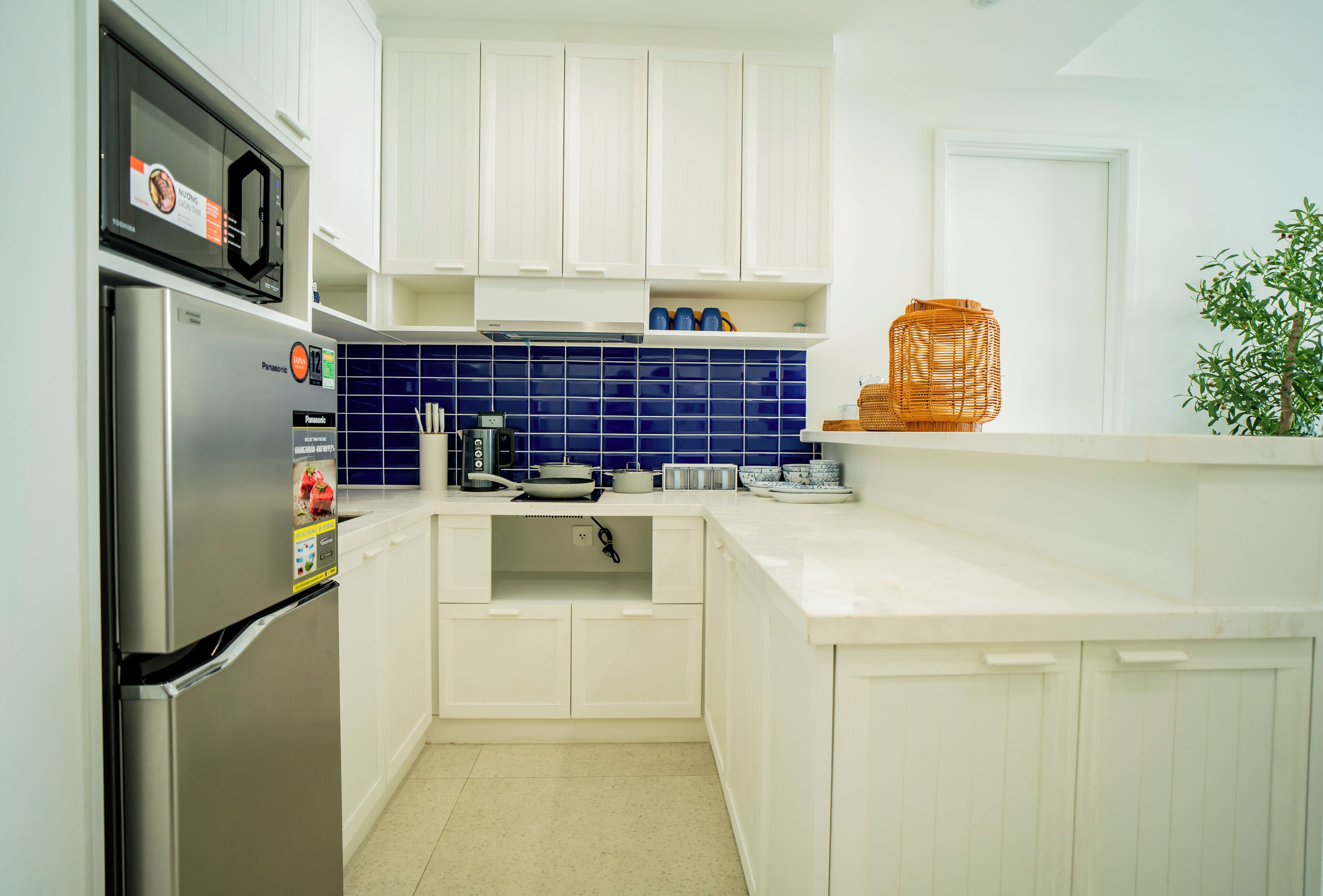 A modern kitchen with white cabinets, a stainless steel refrigerator, a microwave, and blue-tiled backsplash.