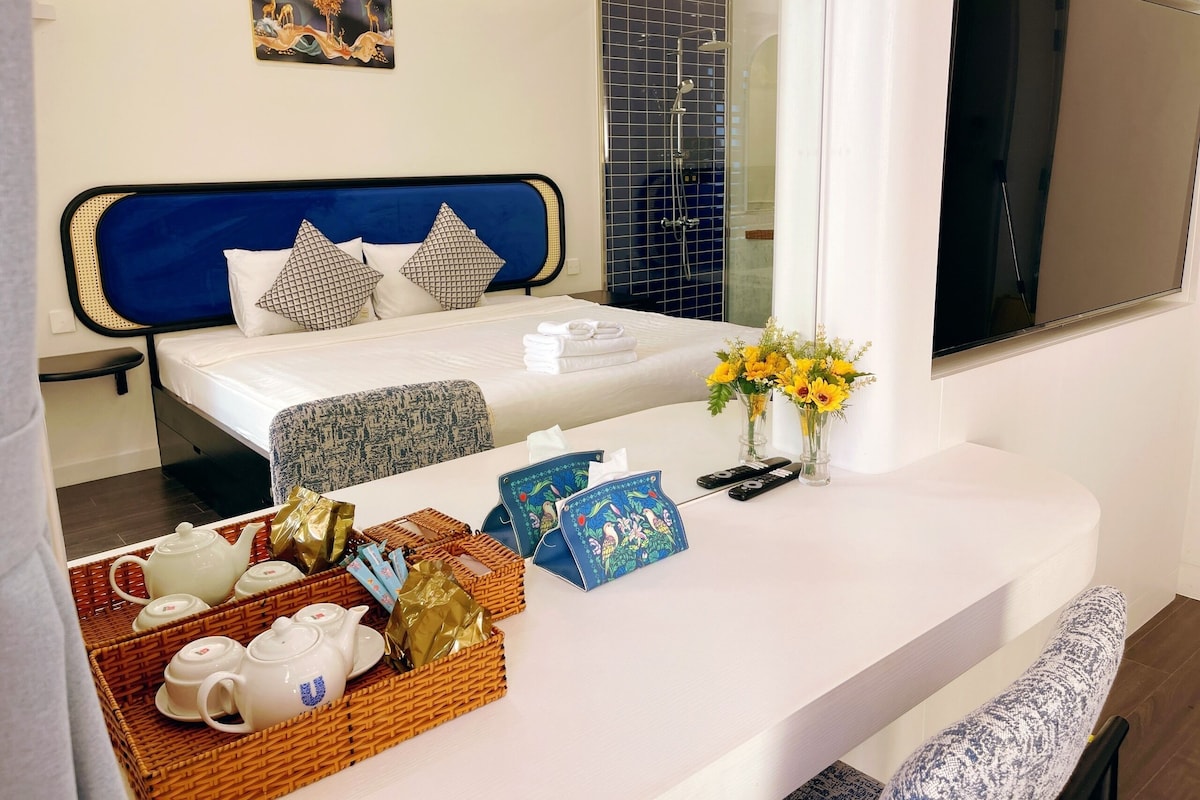 Habitación de hotel con cama, mesita de noche con juegos de té, televisión y zona de ducha.