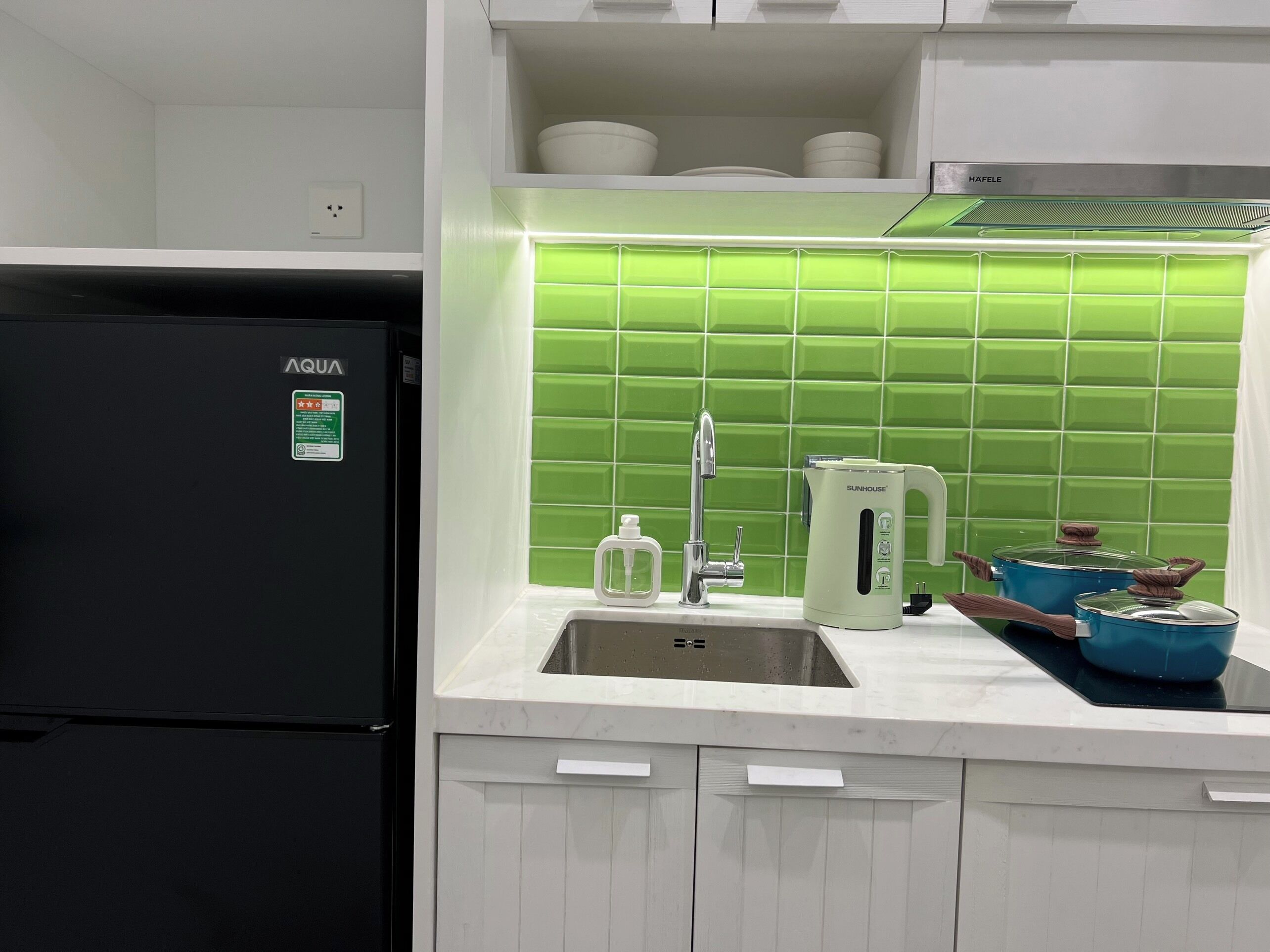 A kitchen with a black refrigerator, a sink, a green tiled backsplash, and a white countertop.