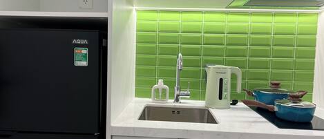 A kitchen with a black refrigerator, a sink, a green tiled backsplash, and a white countertop.