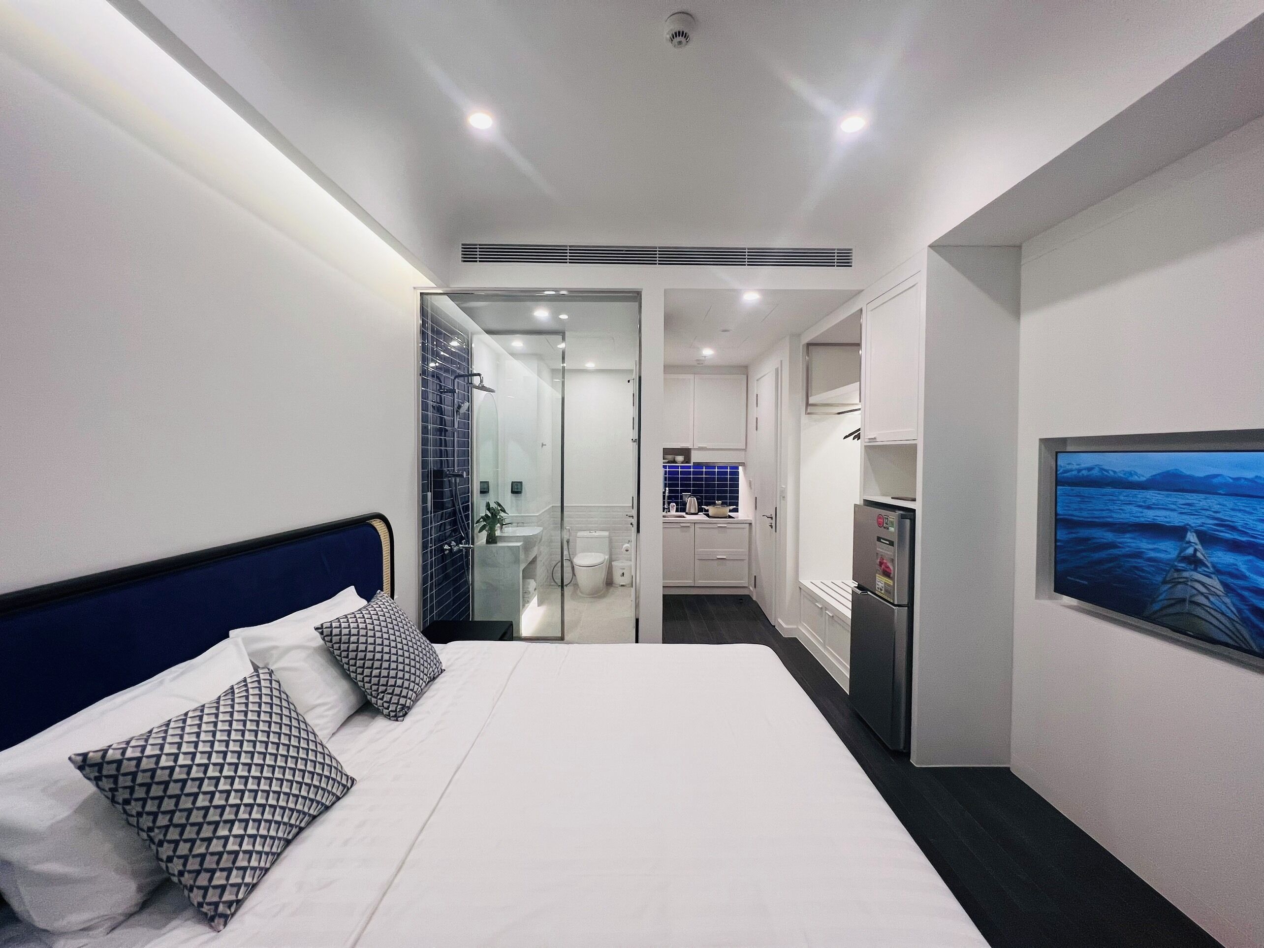 Habitación de hotel con cama, televisión, refrigerador y baño visible a través de una puerta abierta.