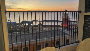 Un balcón con mobiliario de mimbre, vista al frente de un muelle con edificios y una torre del reloj.