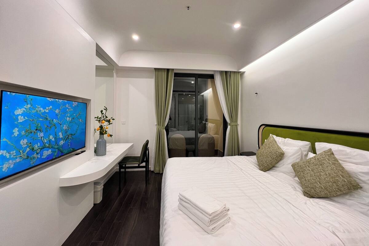 Ein Hotelzimmer mit Bett, Schreibtisch, Flachbildfernseher, Stuhl und Blick durch eine Glastür nach draußen.