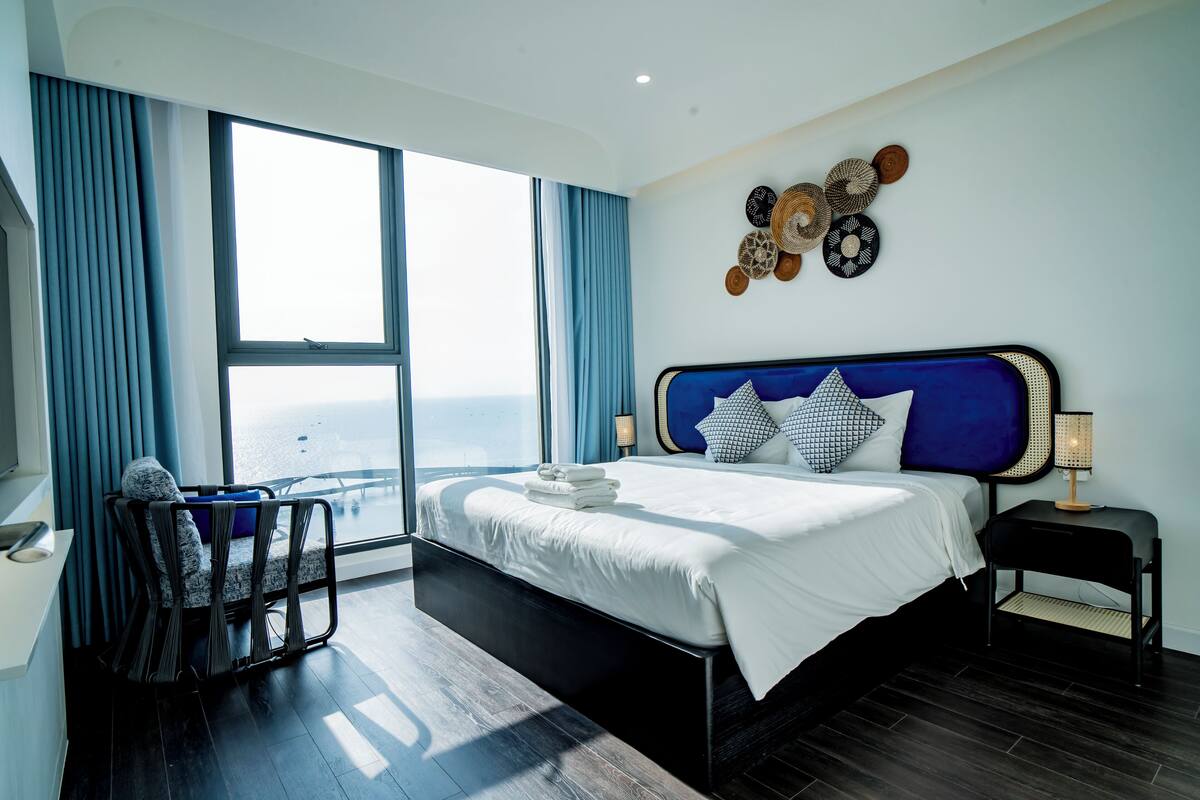 Ein modernes Hotelzimmer mit einem großen Bett, Blick auf die Stadt und einem Balkon mit einem Sessel.