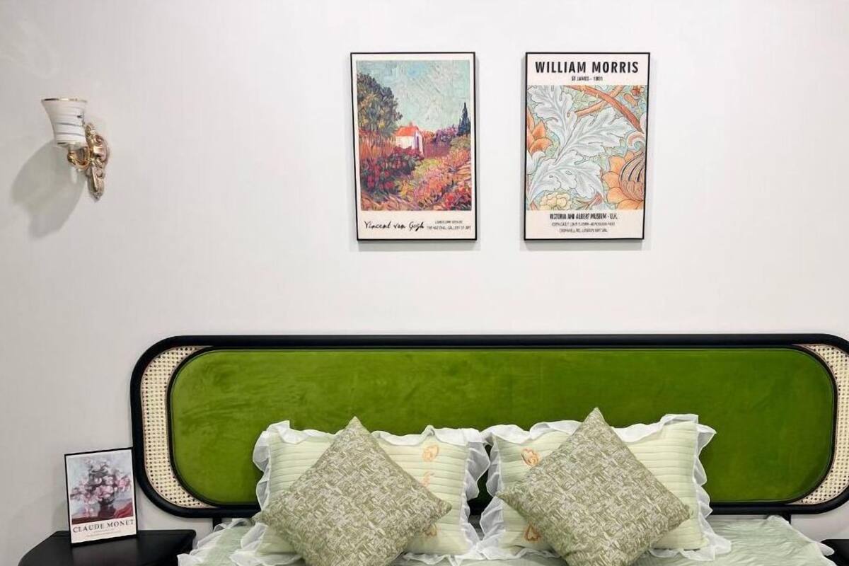 Ein Schlafzimmer mit einem grünen gepolsterten Kopfteil, einem Bett mit einer hellgrünen Bettdecke und zwei gemusterten Kissen sowie zwei gerahmten Kunstwerken an der Wand.