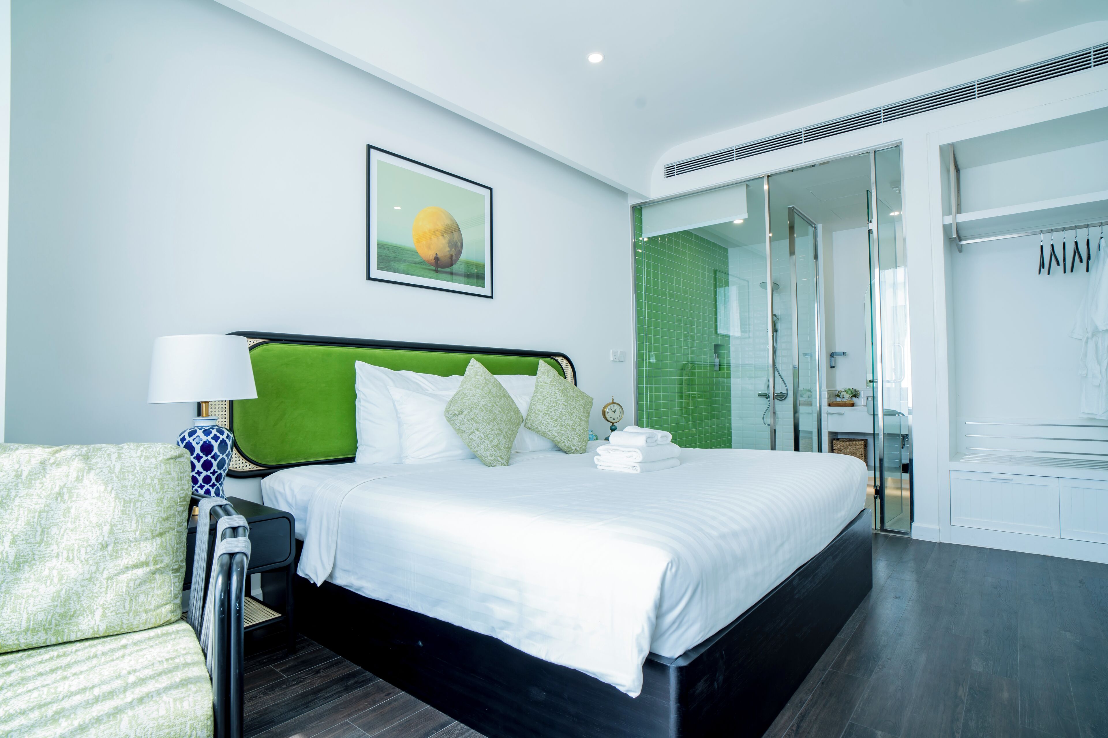 A modern hotel room with a large bed, a green headboard, and a glass shower area.