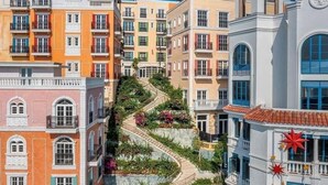Un edificio de varios pisos con una escalera en espiral rodeada de vegetación, con balcones y una torre de campanas.