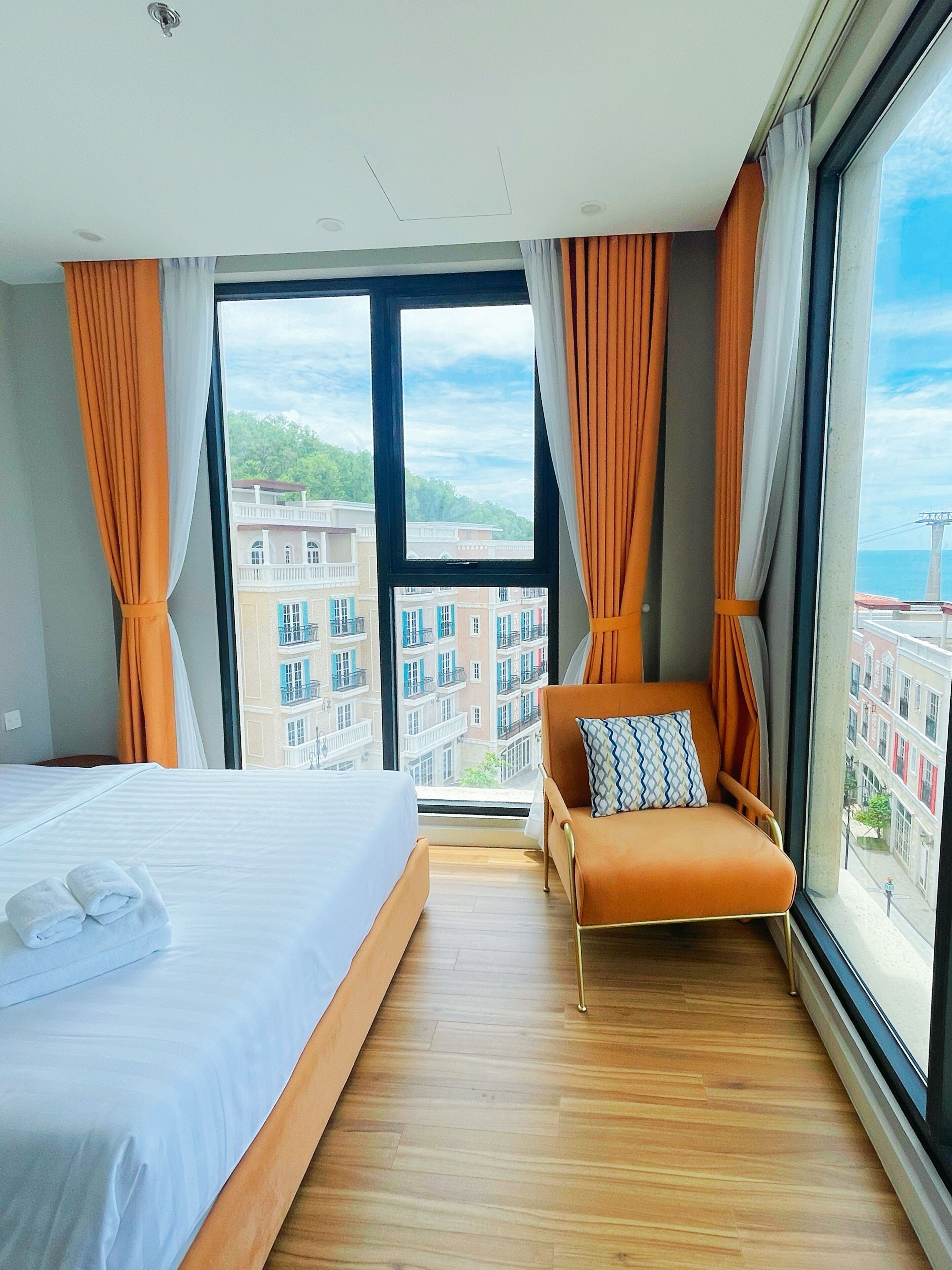 A hotel room with a large bed, a sofa, and a view of buildings through a large window.
