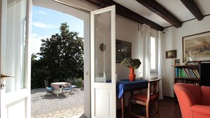 Puerta abierta que da a un patio con mesa y sillas, una estantería llena de libros y un cuadro en la pared.