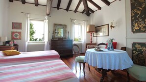 Una habitación con dos camas, un aparador de madera, una mesa con un jarrón de flores y una ventana con cortinas.
