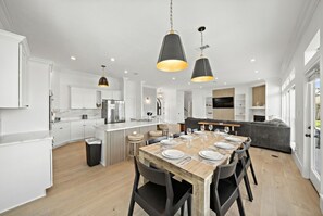 A modern kitchen with white cabinetry, a wooden dining table set for six, and pendant lighting. - Fisherman’s Dream: Canal Front Home & Views (Surfside)