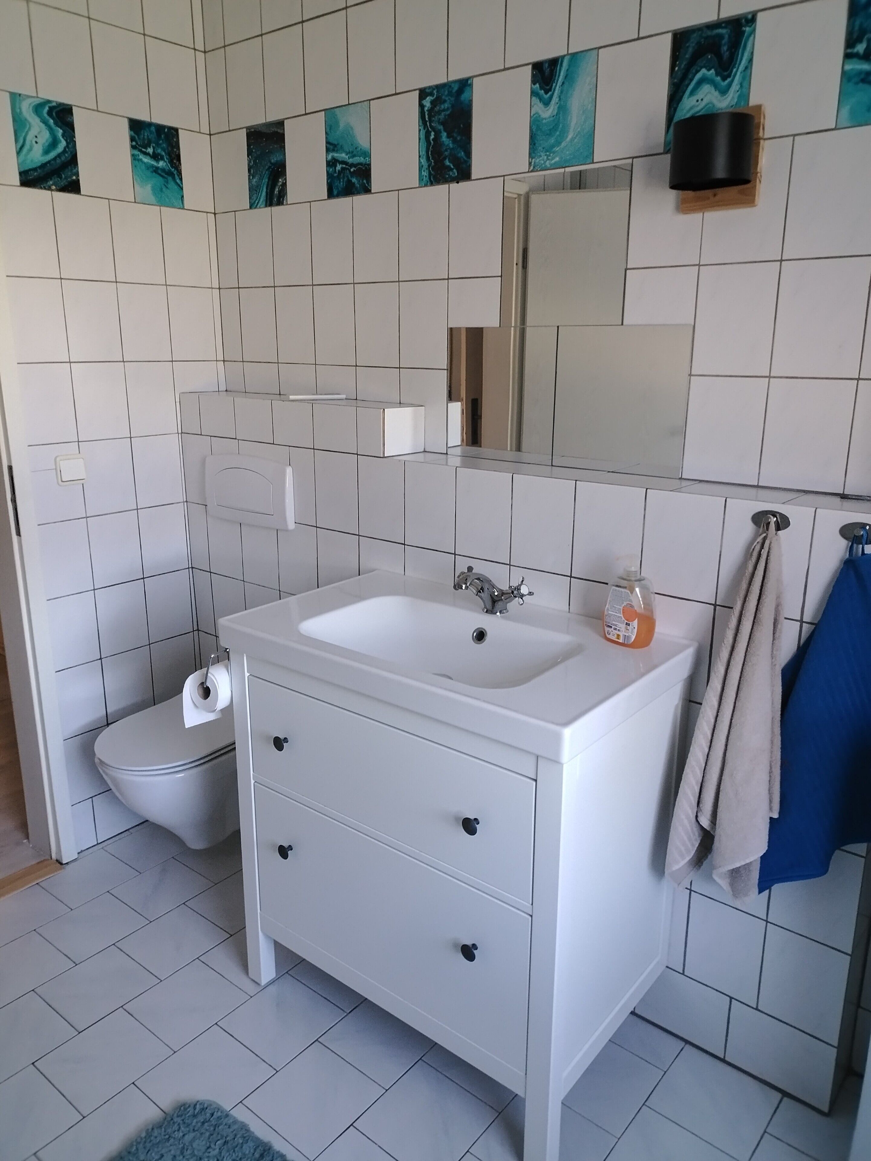 A bathroom with a white sink, a mirror, a toilet, and a blue towel hanging on the wall.