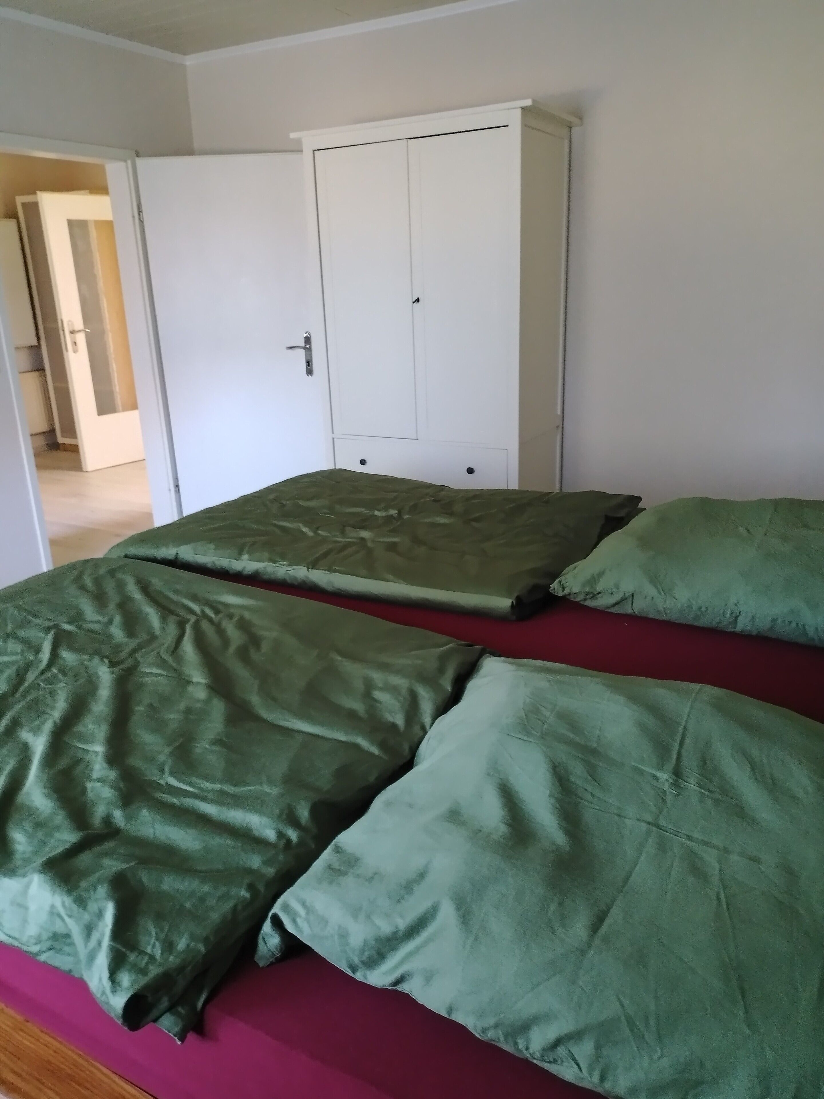 A room with a bed, green bedding, a white wardrobe, and a door leading to another room.