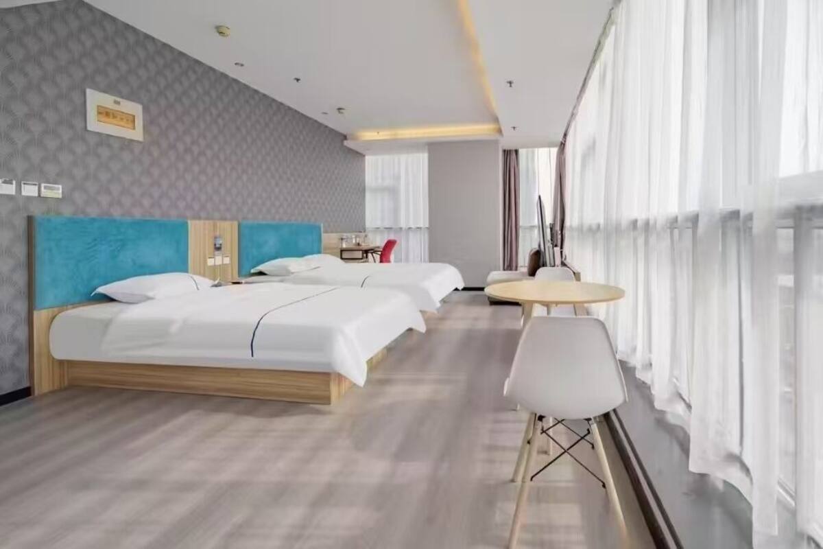 Ein Hotelzimmer mit einem großen Bett, einem kleineren Bett, einem runden Tisch und einem Stuhl.