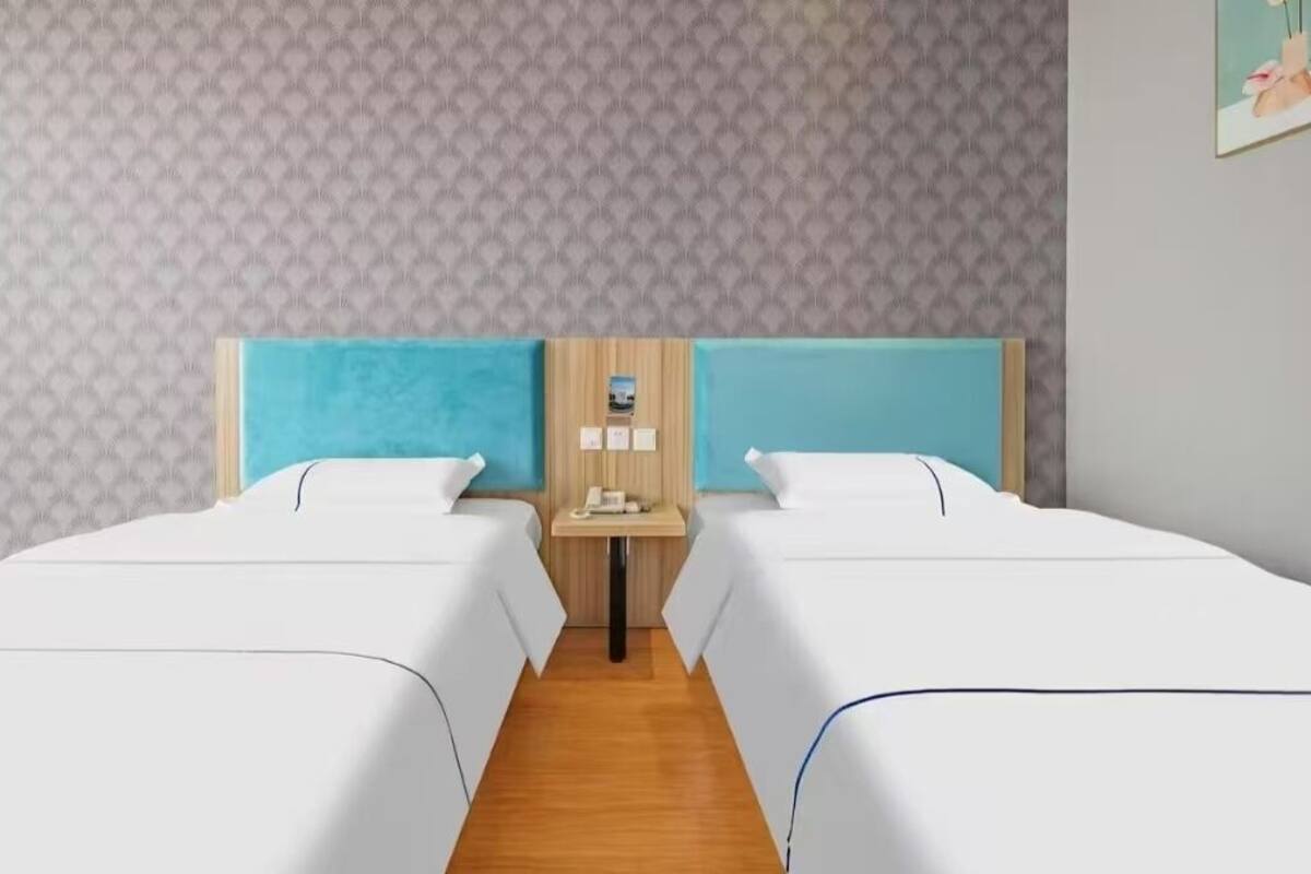 Ein Hotelzimmer mit zwei Einzelbetten, einem Nachttisch aus Holz mit Telefon und einer Wand mit Musterung.