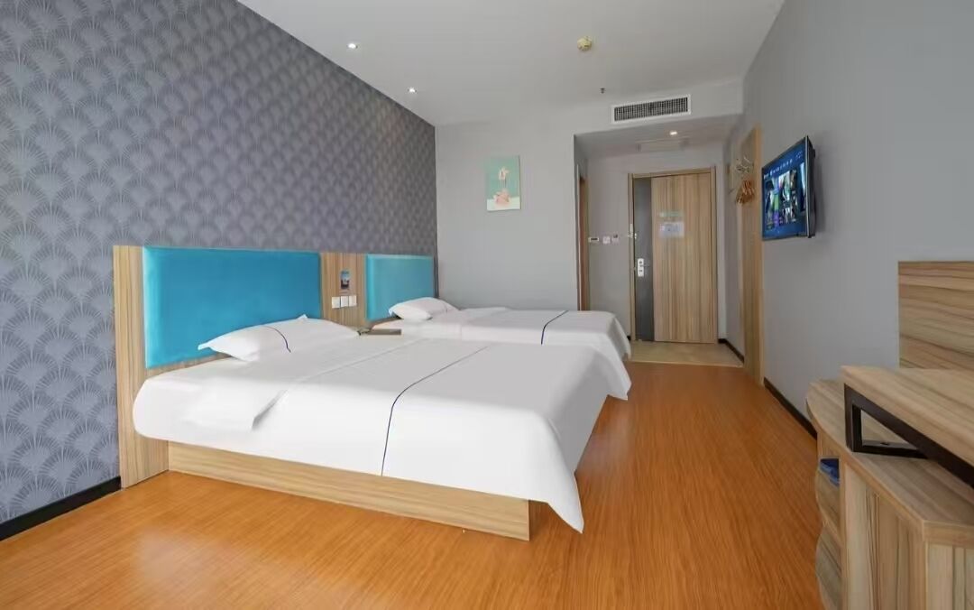 Une chambre d’hôtel avec deux lits, un plancher en bois, un mur décoré et un téléviseur fixé au mur.