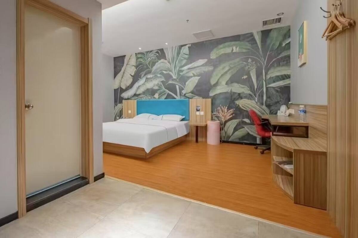 Ein Schlafzimmer mit einem Bett, einem Schreibtisch und einer großformatigen Wandmalerei mit tropischen Blättern.