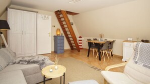 Una sala de estar acogedora con un sofá, una pequeña mesa redonda y un comedor con una mesa y sillas de madera. Una escalera con barandilla de madera conduce a un nivel superior.