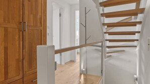 Un interior moderno con una escalera de madera, barandilla de vidrio y un mueble de madera.