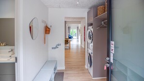 Ein Hotelkorridor mit einem Badezimmer links, einer Bank, einem Waschbereich mit einer Waschmaschine und einem Essbereich im Hintergrund.