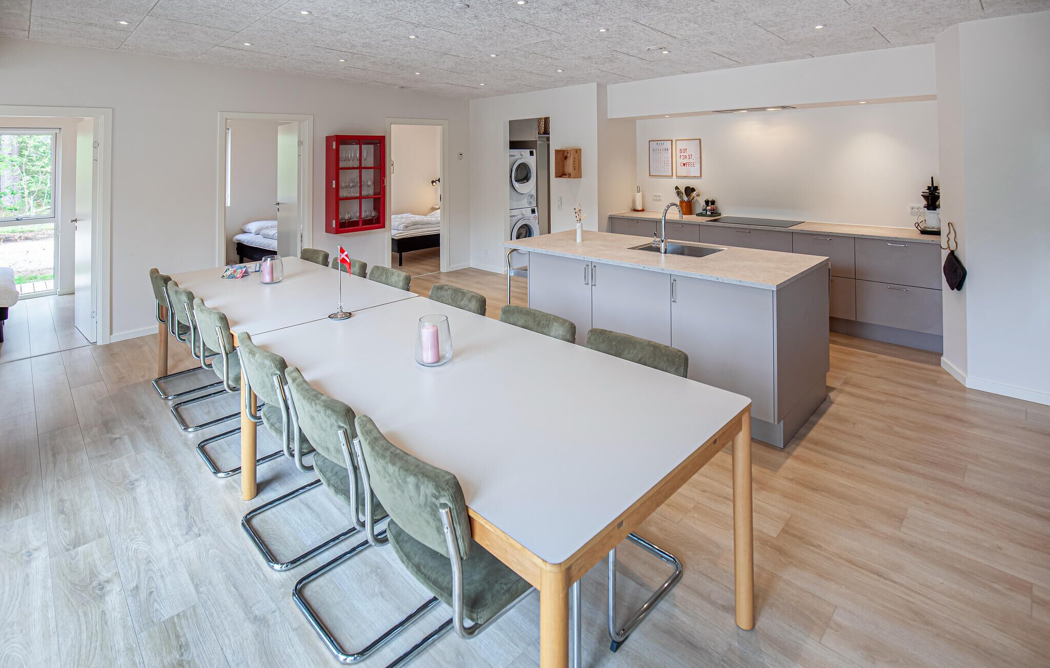 Une cuisine moderne dotée d’un îlot central, d’un coin repas avec une longue table et des chaises, ainsi qu’un espace buanderie avec un lave-linge.