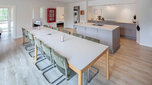 Eine moderne Küche mit einer zentralen Kochinsel, einem Essbereich mit einem langen Tisch und Stühlen sowie einer Waschküche mit einer Waschmaschine.