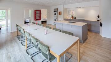 Une cuisine moderne dotée d’un îlot central, d’un coin repas avec une longue table et des chaises, ainsi qu’un espace buanderie avec un lave-linge.