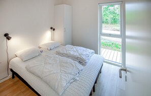 A bed with white bedding, a wall-mounted light, and a window with a view of greenery. - Amazing home in Ebeltoft with sauna (Ebeltoft)