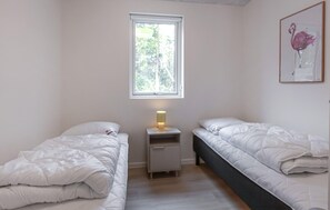A bedroom with two beds, a nightstand with a lamp, a window with a view of trees, and a framed picture on the wall. - Amazing home in Ebeltoft with sauna (Ebeltoft)