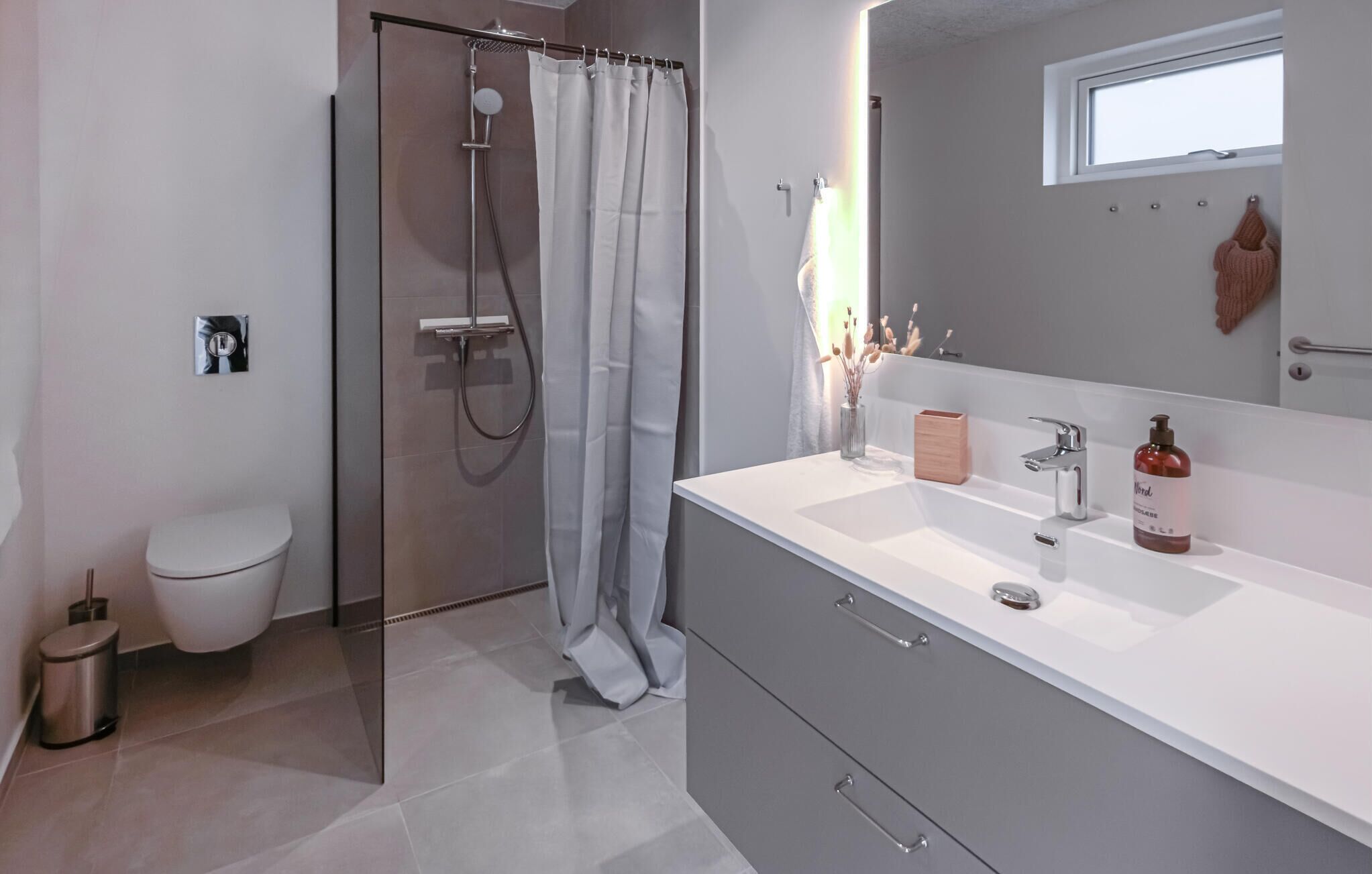 Une salle de bain moderne équipée d’une douche, de toilettes et d’un meuble-lavabo avec un miroir.