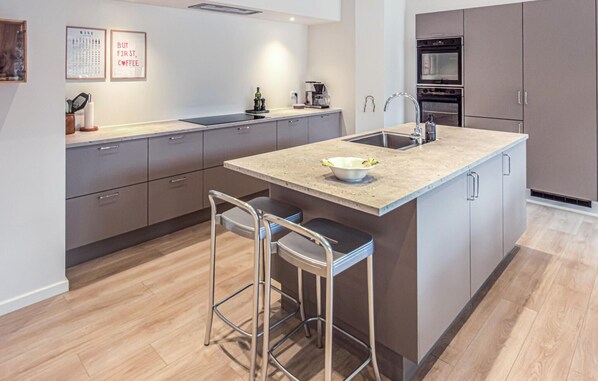 Una cocina moderna con una isla central, taburetes de bar, horno empotrado y cafetera.